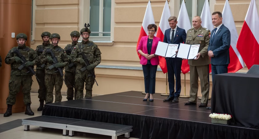 Zdjęcie: 24 lipca 2023 r, podpisanie listu intencyjnego w sprawie utworzenia w Legnicy bazy szkoleniowo-ćwiczeniowej dla Sił Zbrojnych RP. Po prawej stronie ówczesna marszałek Sejmu Elżbieta Witek, ówczesny prezes LSSE Przemysław Bożek, gen. bryg.  Maciej Klisz - dowódca WOT - i Mariusz Błaszczak, ówczesny minister obrony. Fot. MON
