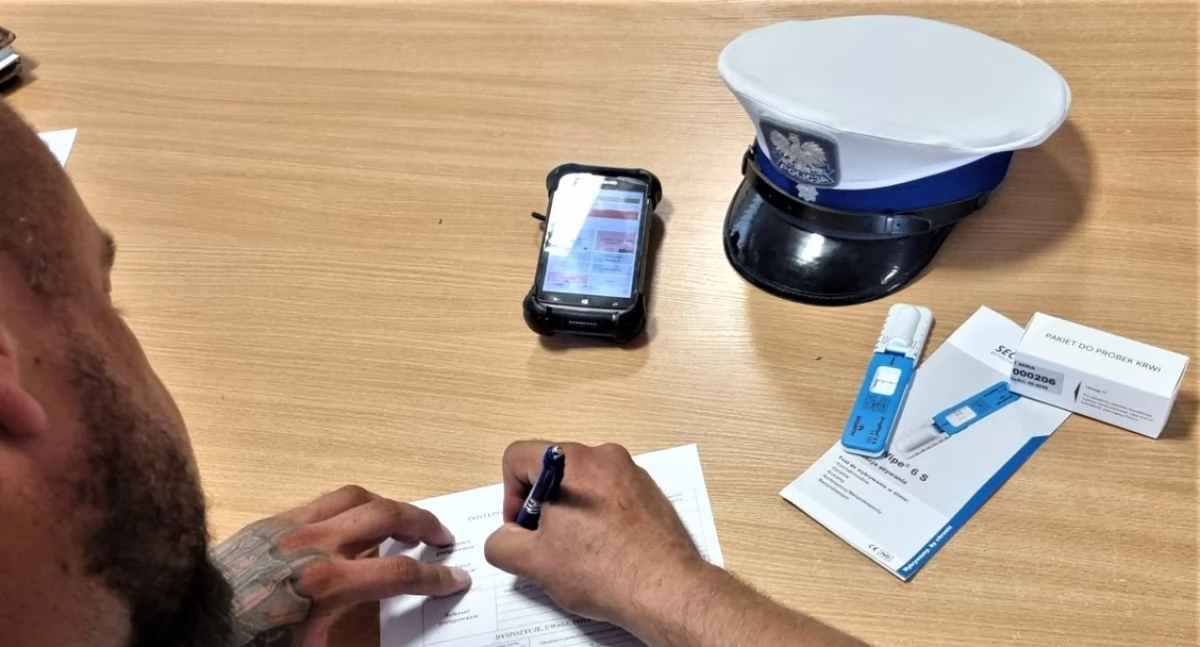 Zdjęcie: policjant wypełniający dokumenty i test narkotykowy Fot.: KMP